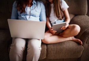 Two women using laptop and tablet on sofa