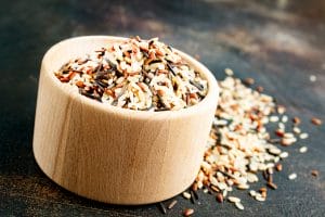 Mixed wild rice in wooden bowl on dark surface
