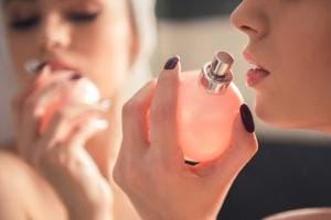 Woman holding pink perfume bottle close to face.
