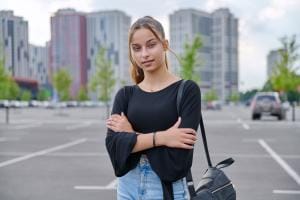 Person standing in parking lot with buildings background.