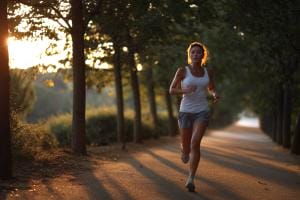 Woman jogging on sunlit forest path