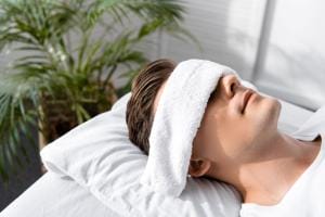 Relaxing man with towel on face near plants.