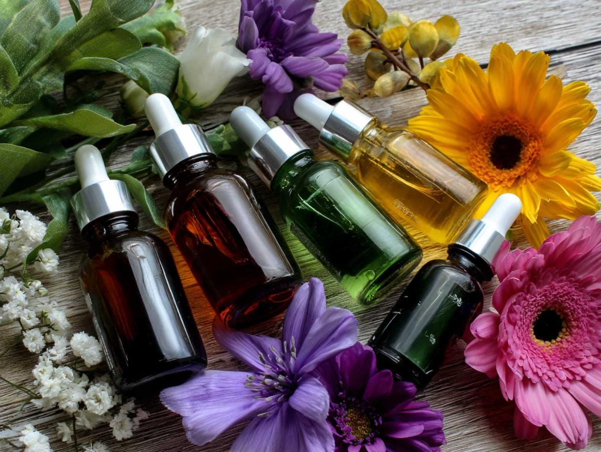 Essential oil bottles with colorful flowers on wood.