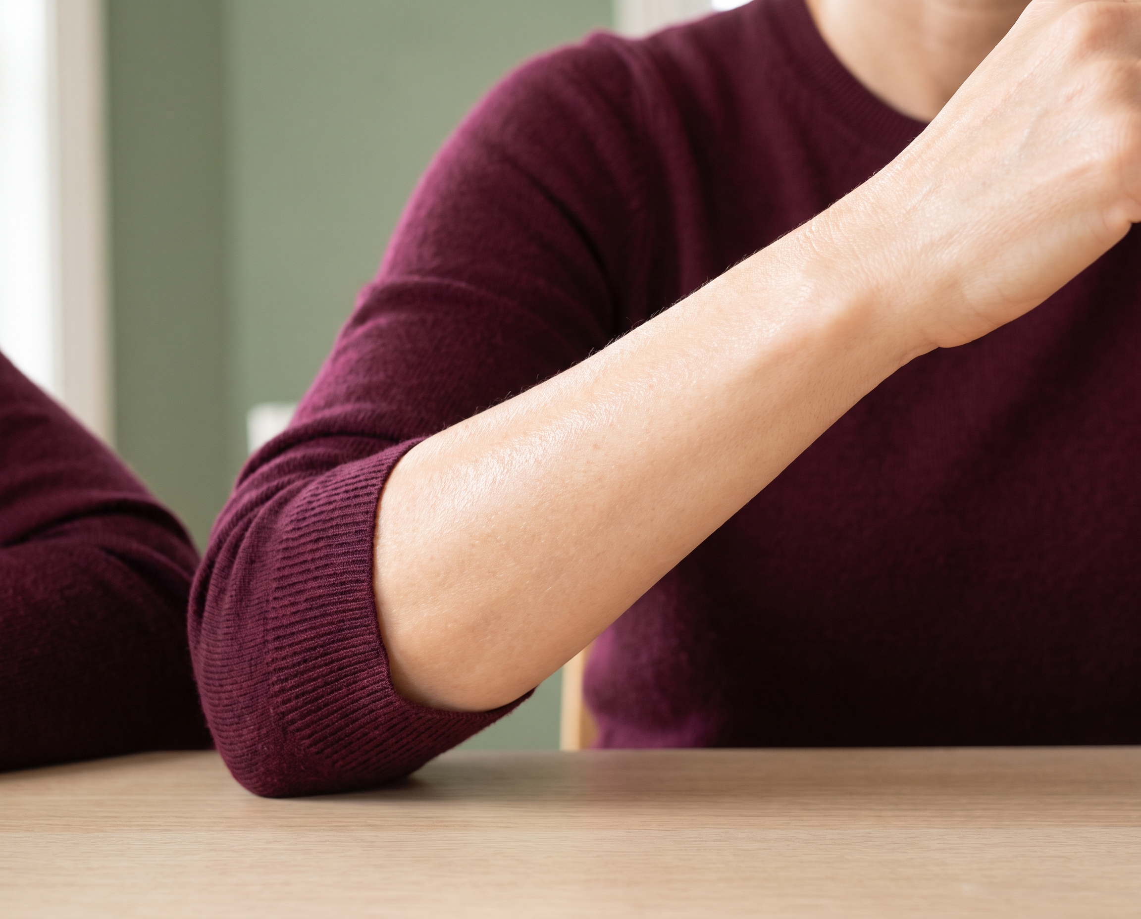 Close-up of smooth, healthy forearm skin against a sage green background