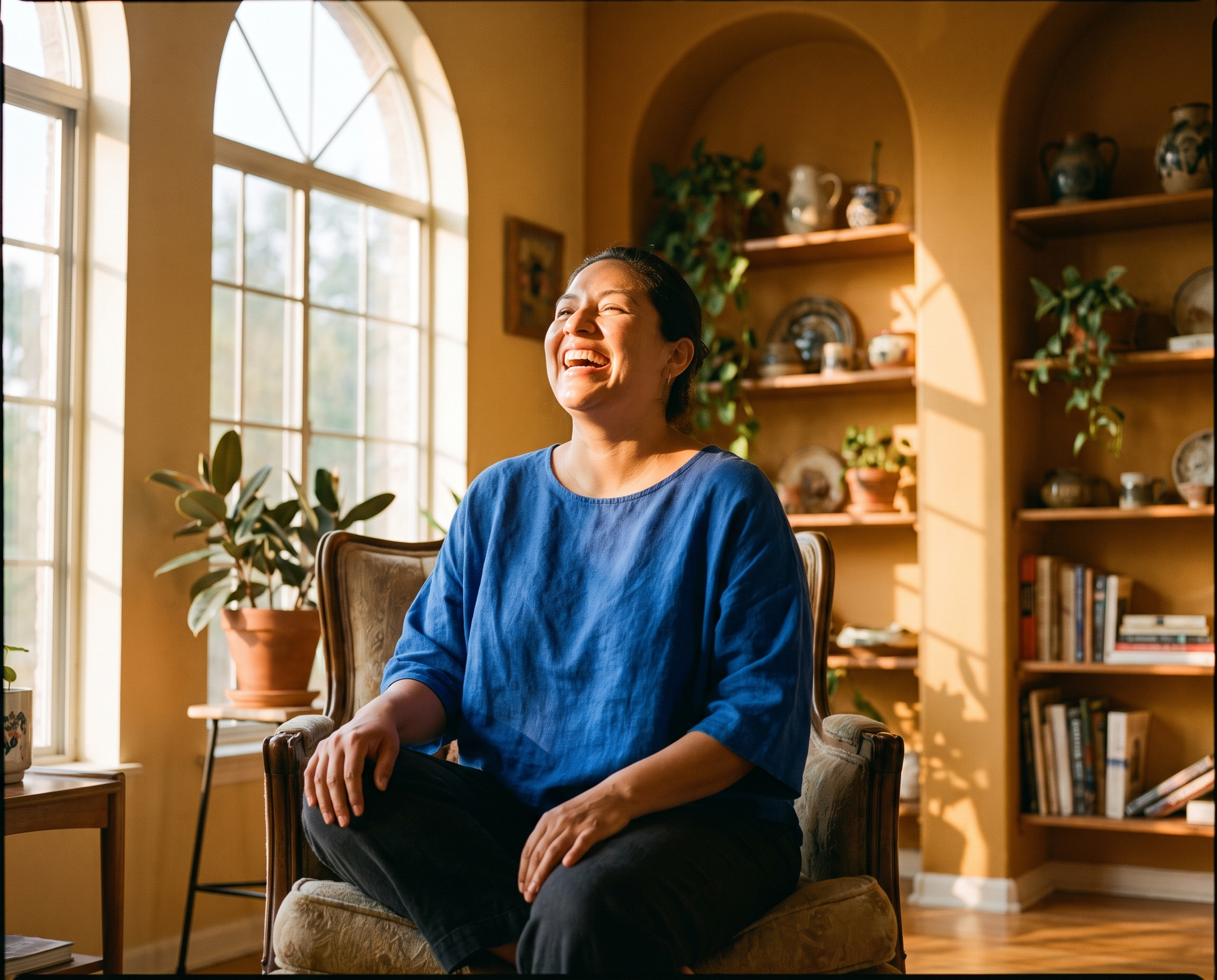 Latina woman laughing in a sun-filled living room with ochre walls and cobalt blue linen top