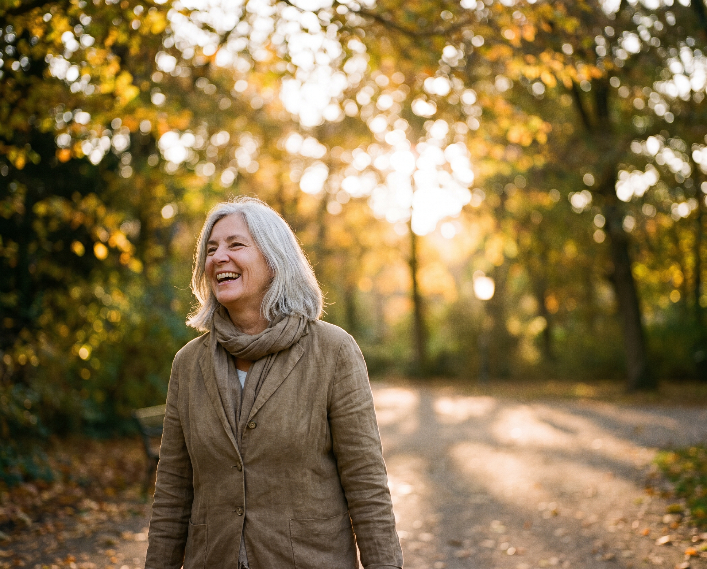 A Caucasian woman in her late 60s laughing outdoors in golden morning light with a luminous complexion