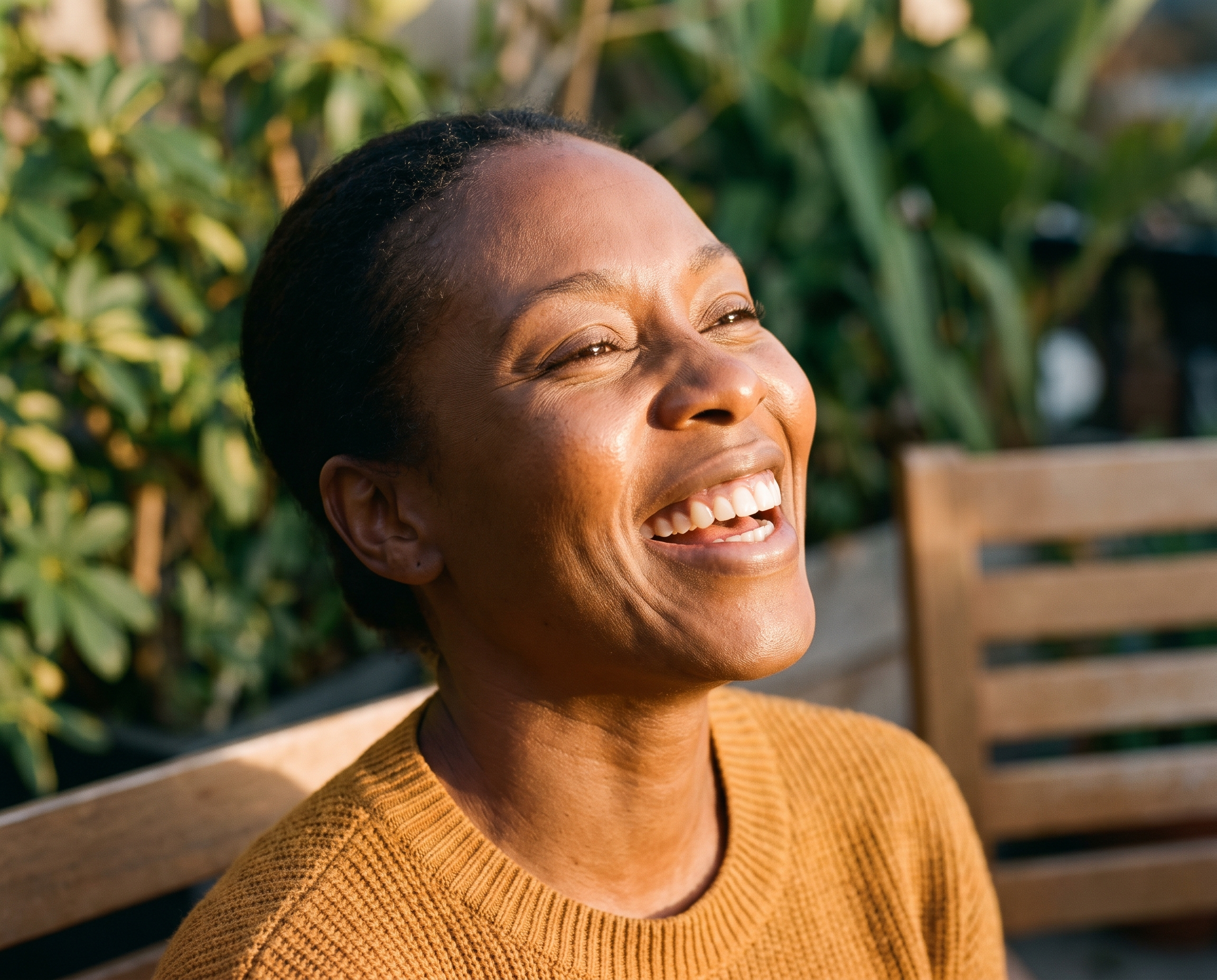 Black woman in her early 40s laughing with face turned into warm golden afternoon sun, skin radiant and textured