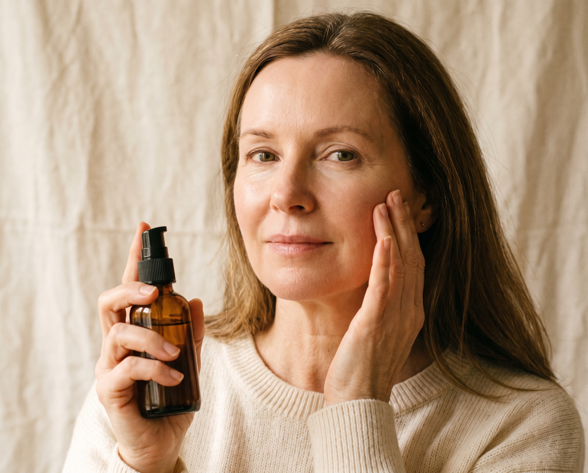 Woman applying facial serum while holding amber pump bottle