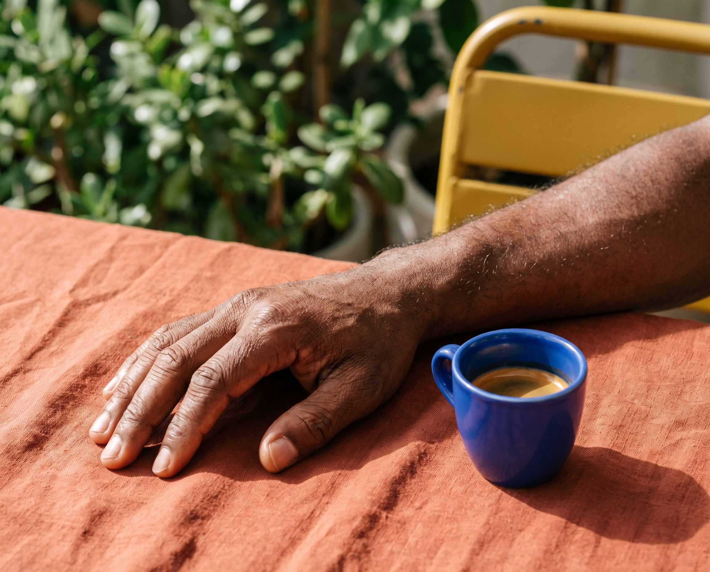 Close-up of a forearm with healthy skin resting beside a blue espresso cup at an outdoor café