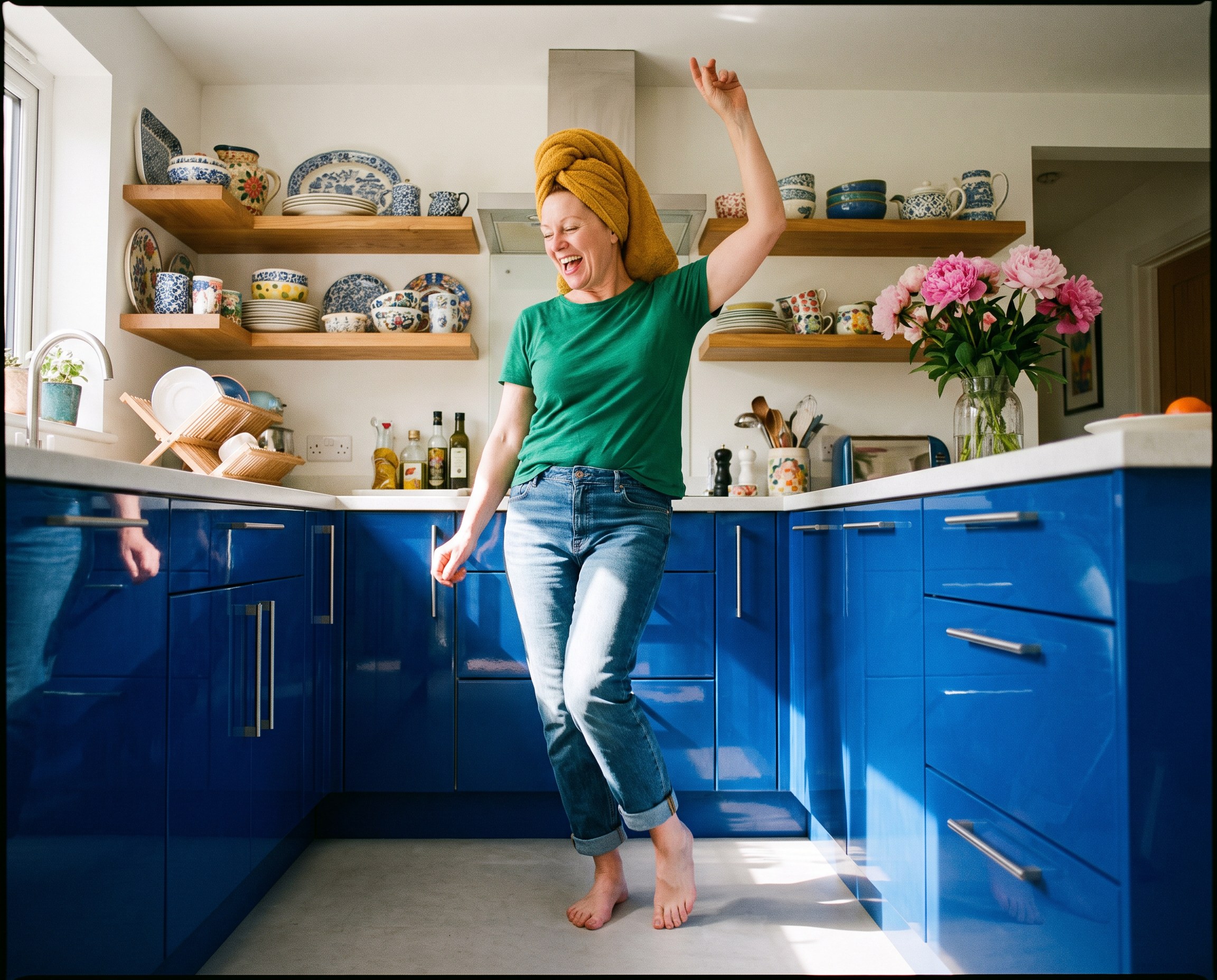 Woman with hair wrapped in a towel dancing in a colorful kitchen while a hair mask sets