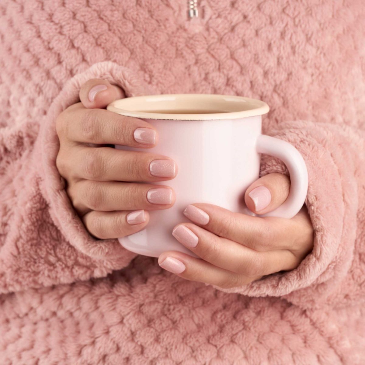 Hands holding a pink mug while wearing a fuzzy robe
