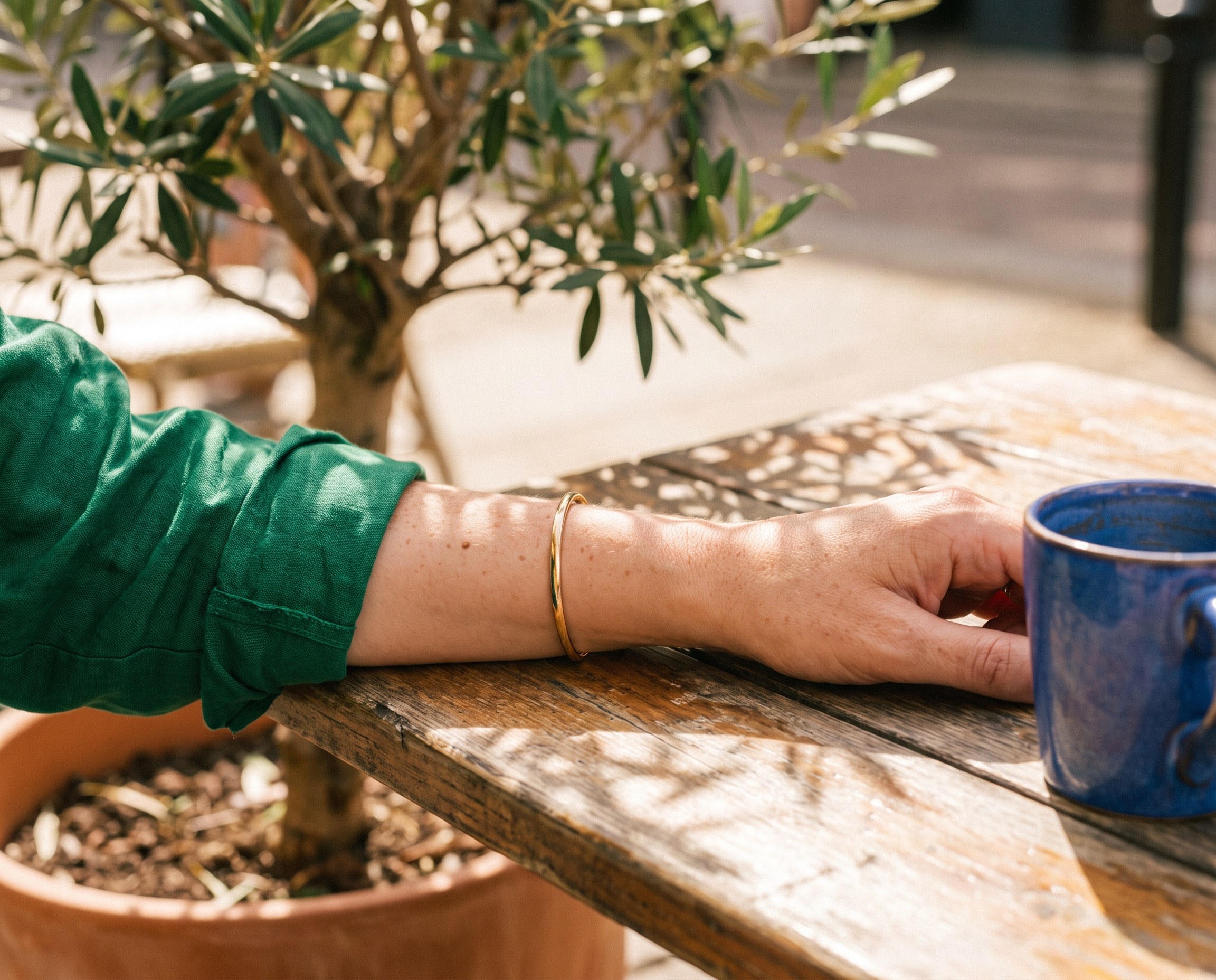 Close-up of a forearm on a sunny cafe table beside a blue coffee cup