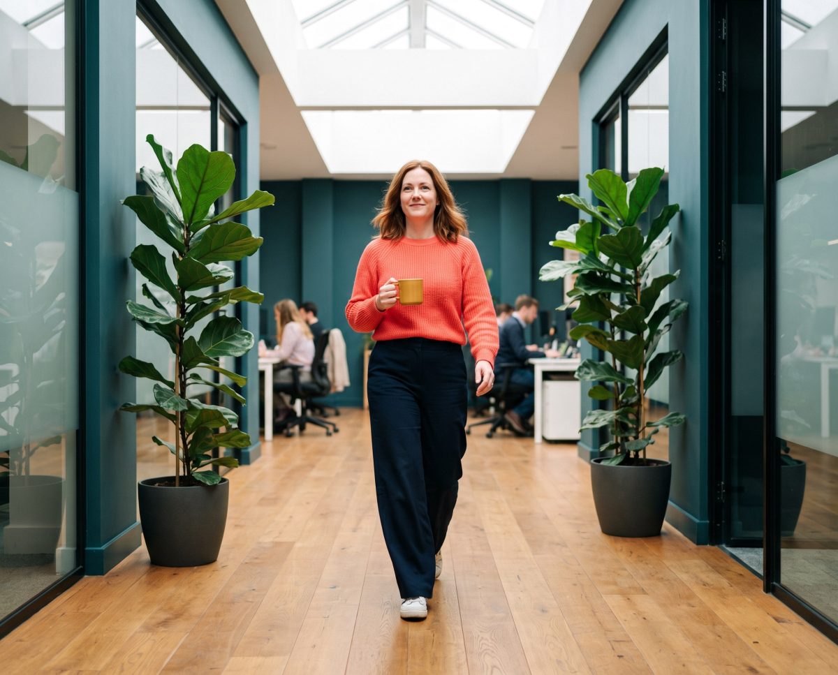 Woman with coffee walks through plant-filled modern office