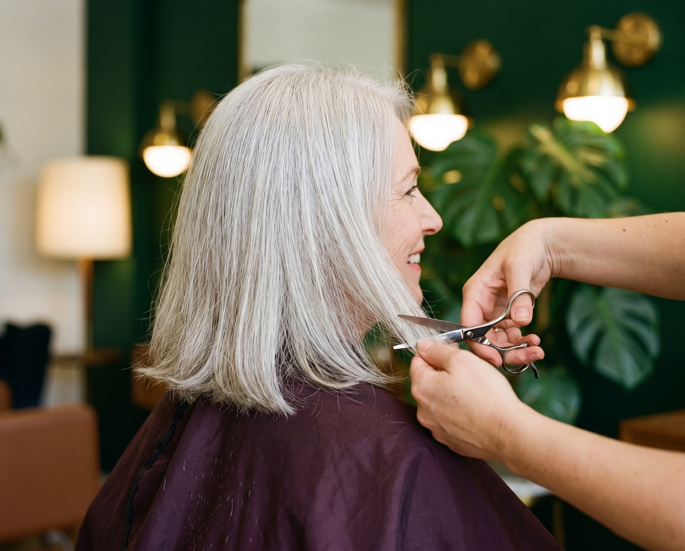 Stylist trimming soft layers into a woman's fine silver hair at a colorful salon
